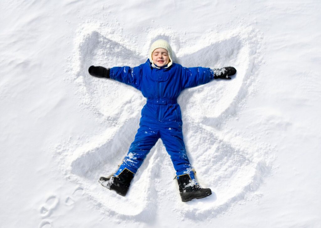A merry student in a blue snow suit makes a snow angel.